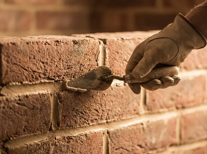 Macro-style illustration of a pointing trowel drawing along a fresh mortar joint between brick courses, held by a single cropped hand, a stylized material study, not a photograph of an actual mason at work